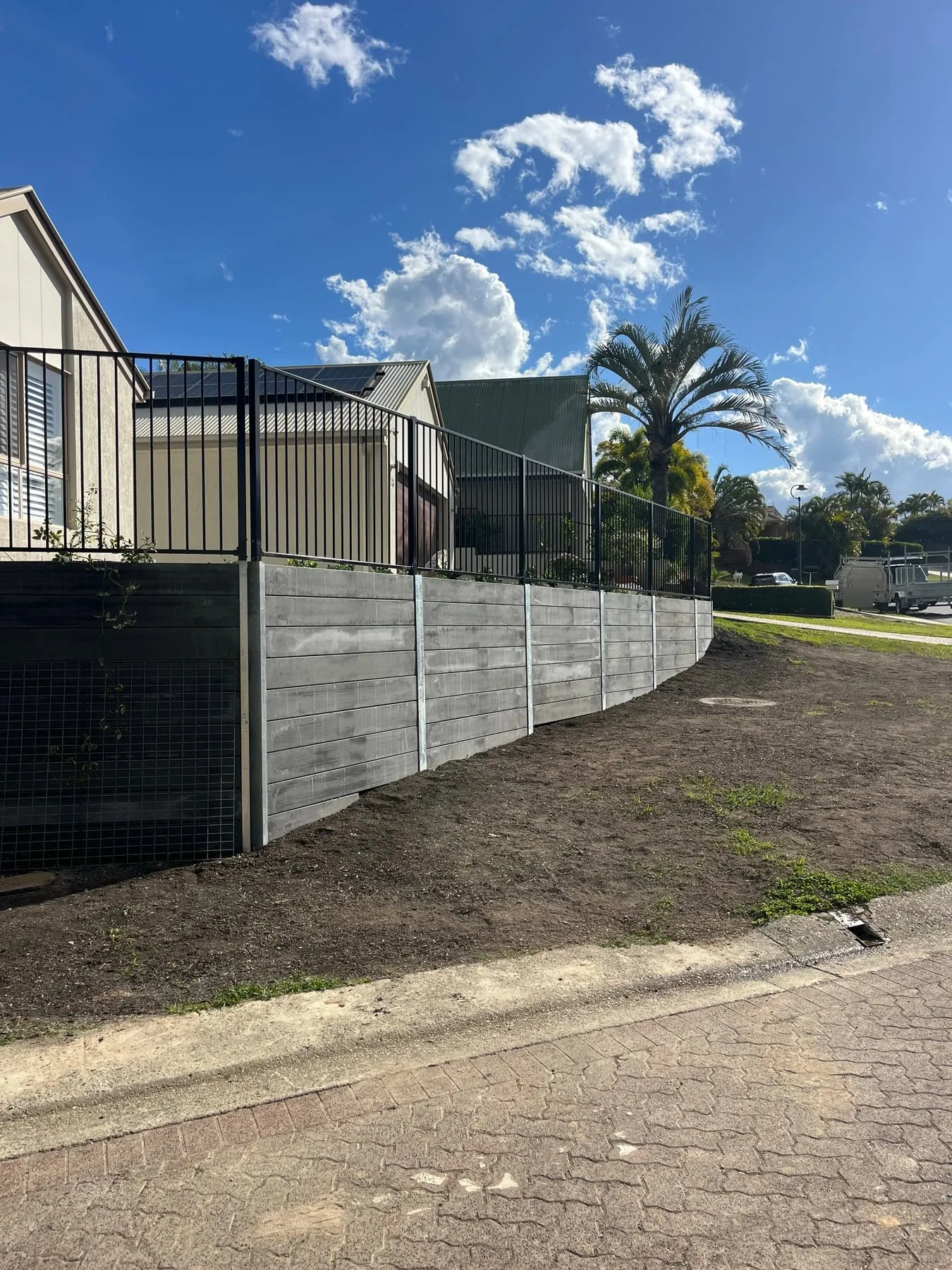 Long curved run of concrete sleeper wall with fencing on top, Albany Creek