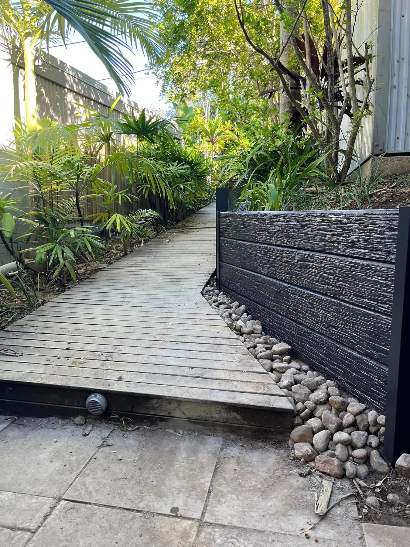 Charcoal woodgrain concrete sleeper wall beside a timber boardwalk