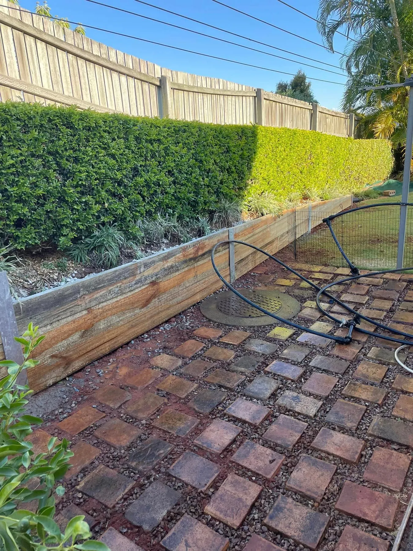Timber sleeper retaining wall behind a clipped hedge and brick paving